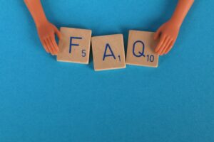 Flat lay of scrabble tiles spelling 'FAQ' with toy hands on a blue background, creating a conceptual image.
